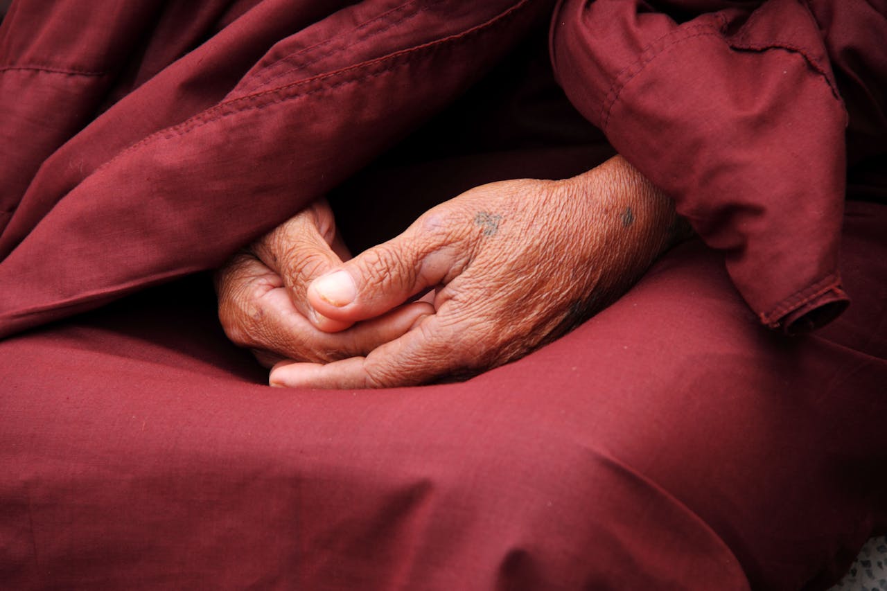 services-04 Close-up of a monk's hands in prayer, wrapped in maroon robe, symbolizing peace and spirituality.
