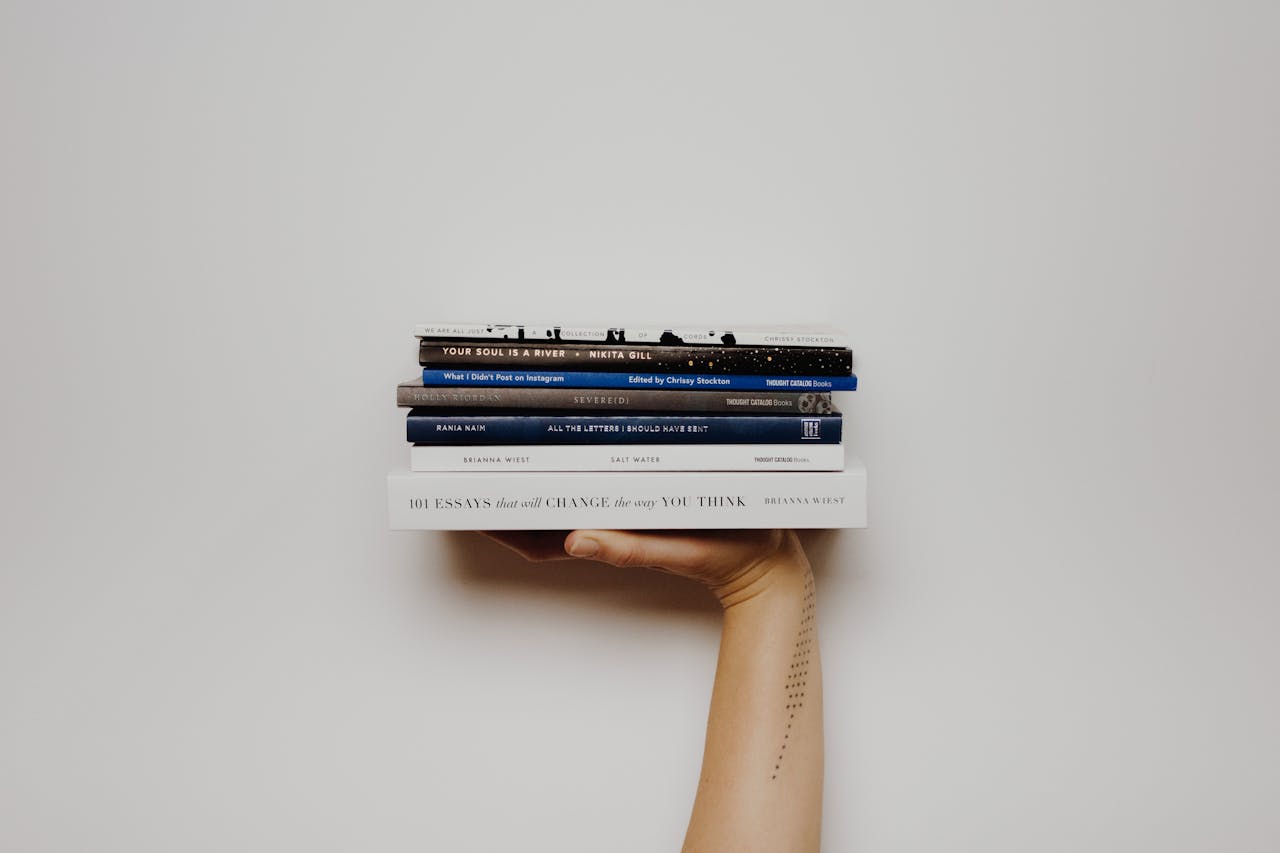 about-img-01 Hand holding a stack of books against a minimal white background, perfect for educational themes.